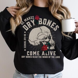 May include: Black sweatshirt with a white skull and red roses. The text reads "He makes dry bones come alive. Ezekiel 37:1-10. Dry bones hear the word of the Lord."