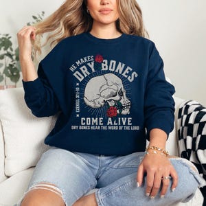 May include: Navy blue sweatshirt with a skull and roses graphic. The text reads "He makes dry bones come alive" and "Ezekiel 37:1-10" and "Dry bones hear the word of the Lord".