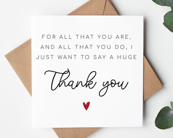 May include: A white card with a brown envelope behind it. The card has black text that reads "FOR ALL THAT YOU ARE, AND ALL THAT YOU DO, I JUST WANT TO SAY A HUGE Thank you" with a small red heart below the text.