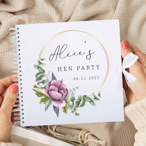 May include: A white spiral bound book with a gold circle frame and floral design. The text "Alice's Hen Party 08.12.2022" is printed on the cover.
