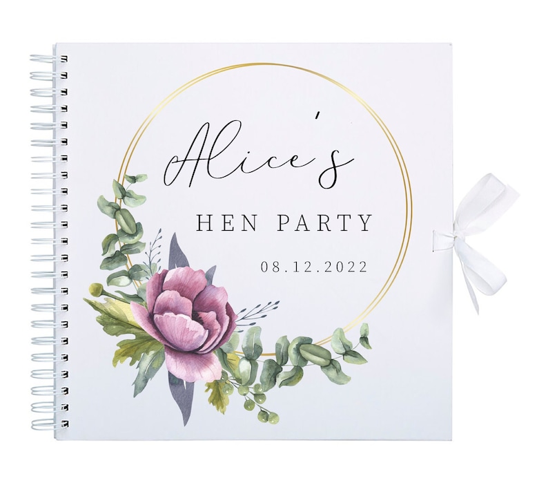 May include: A white scrapbook with a gold circle frame and the text "Alice's Hen Party 08.12.2022". The frame is decorated with watercolor flowers and leaves.