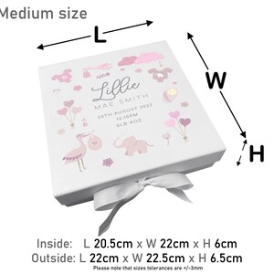 May include: A white gift box with a pink and white design featuring a stork, elephant, and balloons. The box is tied with a white satin ribbon. The box is labeled "Lillie Mae Smith" with the date "20th August 2022" and the time "12:15PM". The box measures 22 cm x 22.5 cm x 6.5 cm.
