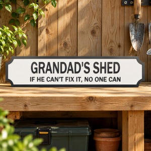 A wooden bench with a sign that reads "GRANDAD'S SHED" and a humorous message below it, surrounded by potted plants and gardening tools.