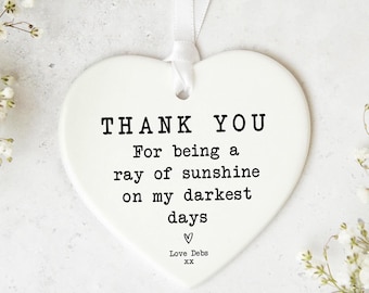 May include: White ceramic heart-shaped ornament with the text "THANK YOU For being a ray of sunshine on my darkest days" and "Love Debs XX" in black lettering.