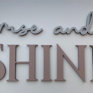 May include: Rise and Shine wall decor with the words "rise" and "and" in light gray and the word "SHINE" in a light brown color.