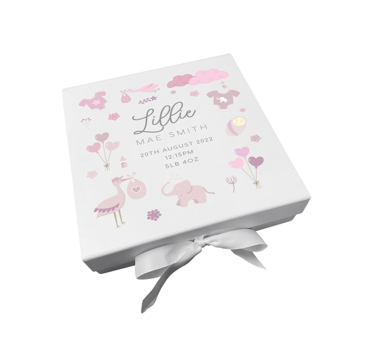 May include: White keepsake box with a pink and white design featuring a stork, elephant, and baby items. The box has a white satin ribbon and is personalized with the name "Lillie Mae Smith", the date "20th August 2022", the time "12:15PM", and the weight "5LB 4OZ".