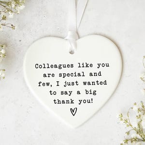 a heart-shaped ornament with a message that says "Colleagues like you are special and few, I just wanted to say a big thank you!" The ornament is surrounded by white flowers, creating a pleasant and thoughtful atmosphere.