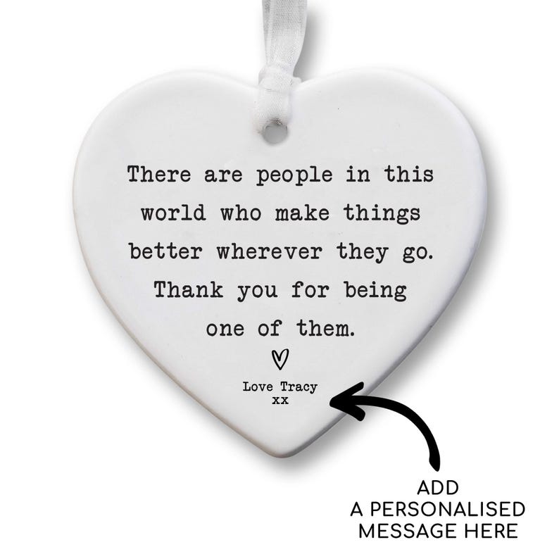 The image is a heart-shaped ornament with a personalized message attached to it. The message reads, "There are people in this world who make things better wherever they go. Thank you for being one of them." The ornament is personalized with the name "Love Tracy" and an arrow pointing to it. The message is a heartfelt expression of gratitude and appreciation.