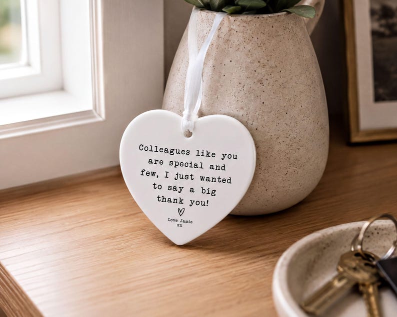 a heart-shaped ceramic tag hanging on a wooden surface, with a potted plant and keys visible in the background.