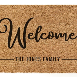 May include: A brown coir doormat with the text "Welcome" in a black cursive font. Below the text is a line with the text "The Jones Family" in black.