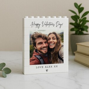 May include: A white block photo frame with the text "Happy Valentines Day!" and a photo of a smiling couple. The bottom of the frame reads "LOVE ALEX XX" with a heart symbol.