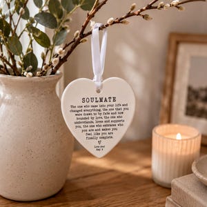 a heart-shaped ornament hanging from a branch, with a candle and a vase of greenery nearby.