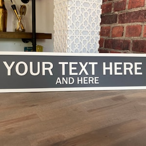 May include: A rectangular sign with rounded corners and a white border. The sign is grey with the text "YOUR TEXT HERE AND HERE" in white lettering.