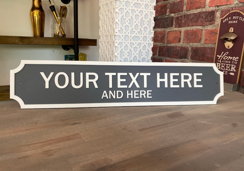 May include: A rectangular sign with rounded corners and a white border. The sign is grey with the text "YOUR TEXT HERE AND HERE" in white lettering.