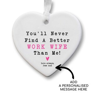 May include: A white heart-shaped ornament with a white ribbon for hanging. The text reads "You'll Never Find A Better WORK WIFE Than Me!" in black and pink. A pink heart and the words "Love always, Jess xxx" are also present.