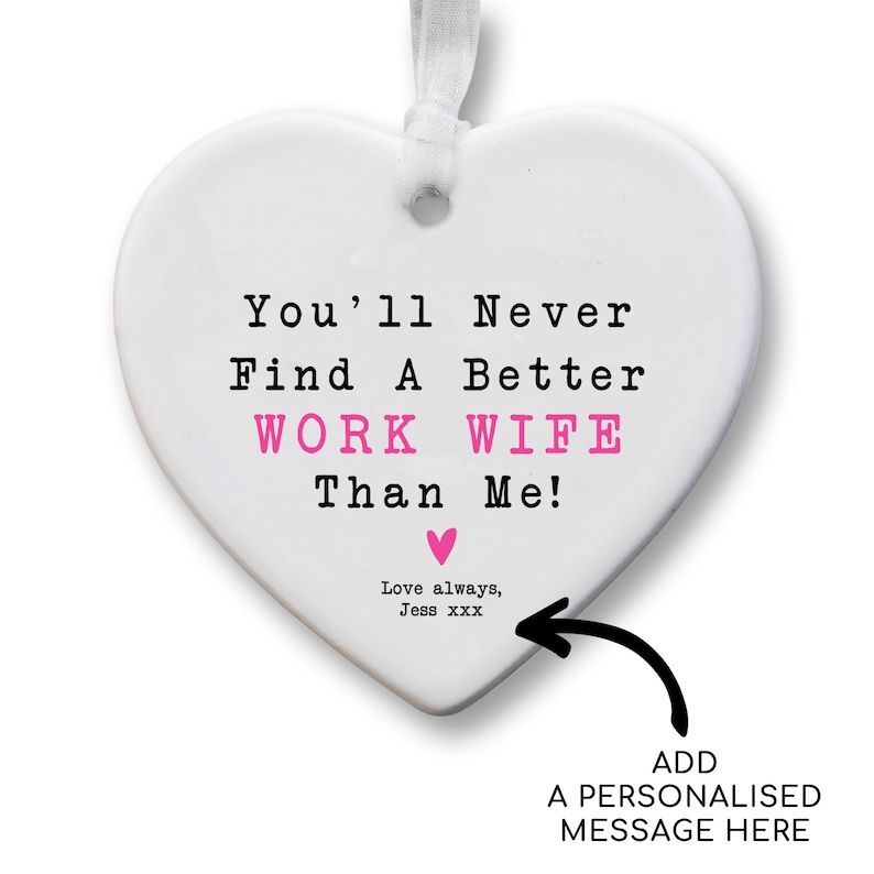 May include: A white heart-shaped ornament with a white ribbon for hanging. The text reads "You'll Never Find A Better WORK WIFE Than Me!" in black and pink. A pink heart and the words "Love always, Jess xxx" are also present.