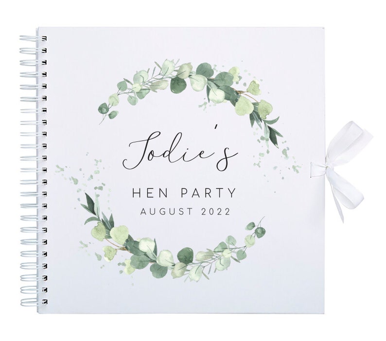 May include: White spiral bound guest book with a green eucalyptus wreath design and the text "Sodie's Hen Party August 2022".