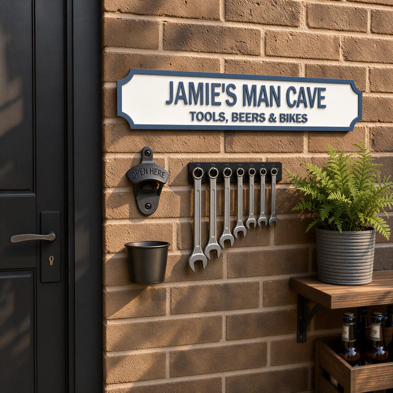 a brick wall with a sign that reads "JAMIE'S MAN CAVE" and a row of tools hanging on it. There is also a potted plant and a beer bottle on the wall.