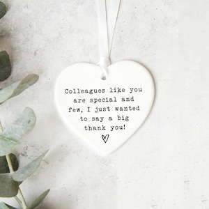 a heart-shaped ornament with a message that says "Colleagues like you are special and few, I just wanted to say a big thank you!" The ornament is placed on a white surface, with some greenery visible in the background.