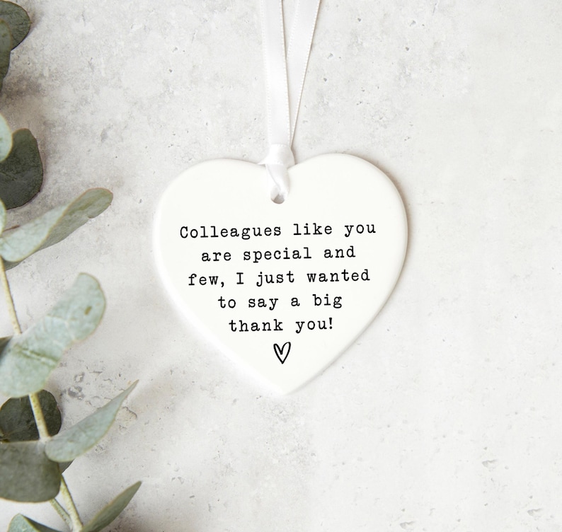 a heart-shaped ornament with a message that says "Colleagues like you are special and few, I just wanted to say a big thank you!" The ornament is placed on a white surface, with some greenery visible in the background.