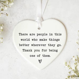 a heart-shaped ornament with a message about appreciating the people who make things better, surrounded by white flowers.