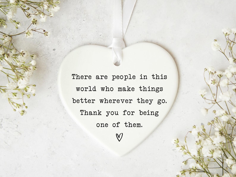 a heart-shaped ornament with a message about appreciating the people who make things better, surrounded by white flowers.