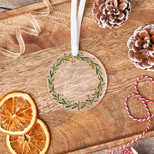 May include: A clear, round Christmas ornament with a white ribbon. The ornament features the text "Christmas 2025" and "The Brown Family" surrounded by a green and red wreath. The names "Mummy, Daddy, Alice, Teddy & Alfie" are also included.