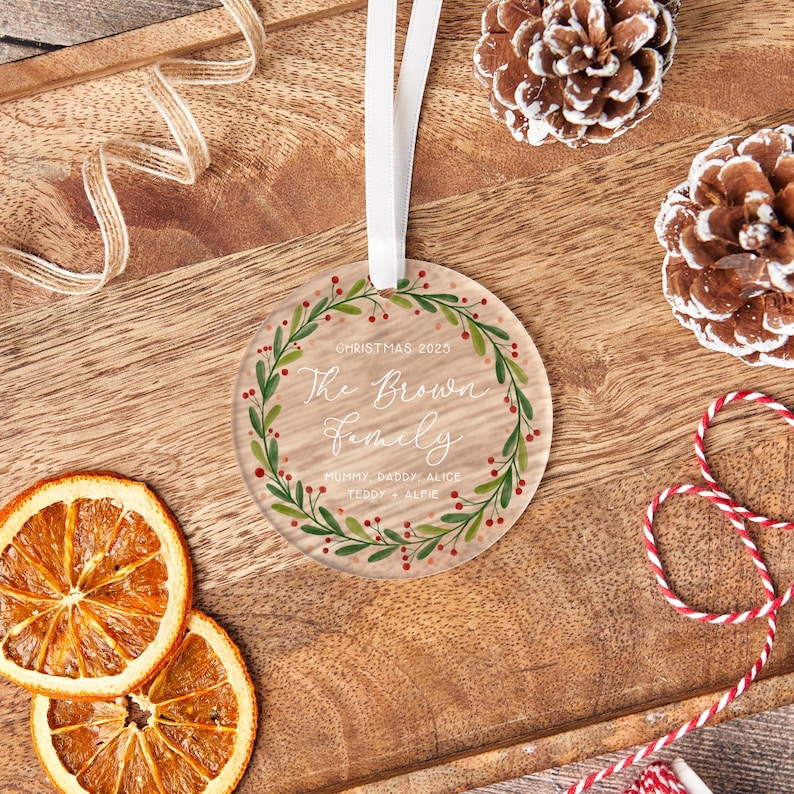 May include: A clear, round Christmas ornament with a white ribbon. The ornament features the text "Christmas 2025" and "The Brown Family" surrounded by a green and red wreath. The names "Mummy, Daddy, Alice, Teddy & Alfie" are also included.
