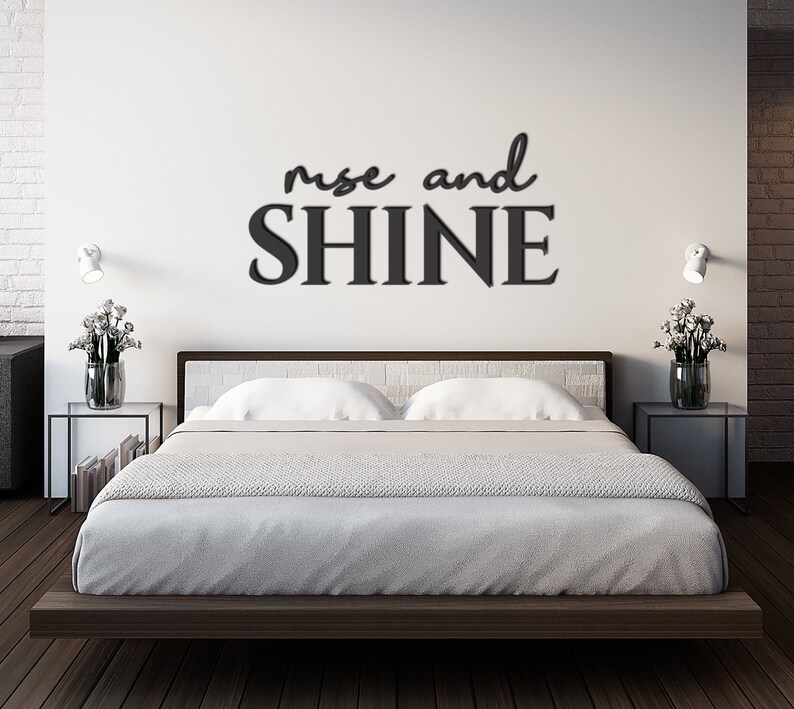May include: A white bedroom with a bed and two nightstands. The wall behind the bed has a black vinyl decal that reads "rise and shine".