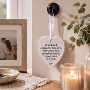 a heart-shaped sign with a romantic message, a framed photo of a couple, a candle, and a plant on a table.