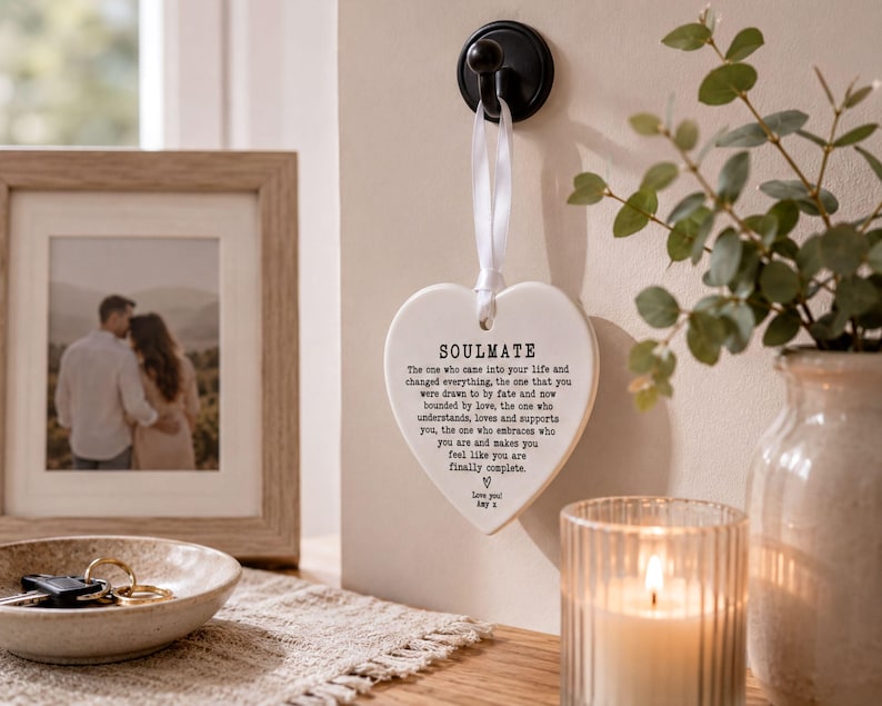 a heart-shaped sign with a romantic message, a framed photo of a couple, a candle, and a plant on a table.
