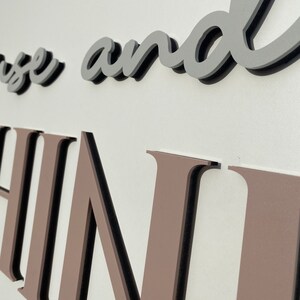 May include: Close-up of a brown and black sign with the words "House and Home" in a cursive font.