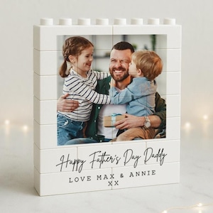 May include: White Lego-style photo block with a photo of a father with two children. The photo shows the father smiling and holding a gift while the children hug him. The text below the photo reads "Happy Father's Day Daddy Love Max & Annie XX".