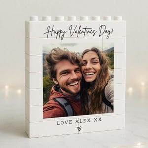 May include: White block photo frame with a picture of a smiling couple. The frame reads "Happy Valentines Day!" in black script. Below the photo, the text "LOVE ALEX XX" is written with a heart symbol.