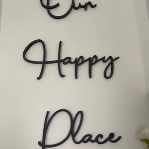 May include: Black cursive script wall decor with the words "Our Happy Place".