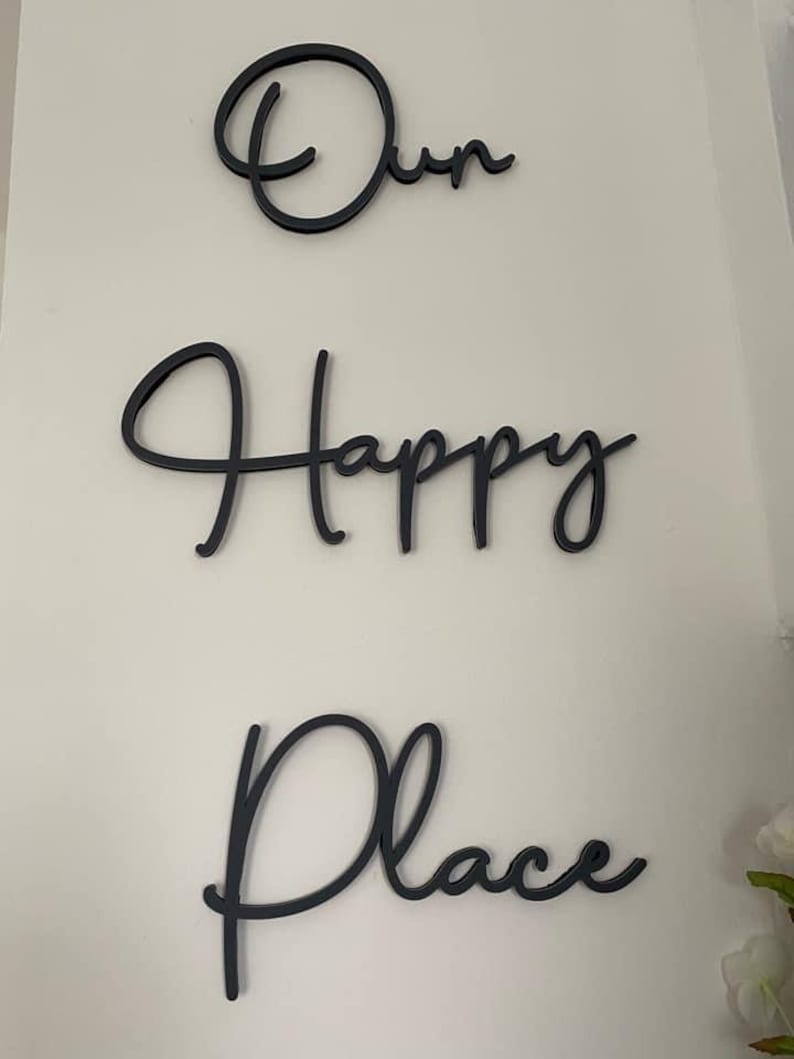 May include: Black cursive script wall decor with the words "Our Happy Place".