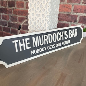 May include: A grey and white sign with the text "The Murdoch's Bar" and "Nobody gets out sober".
