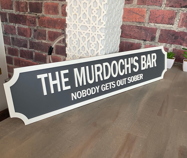 May include: A grey and white sign with the text "The Murdoch's Bar" and "Nobody gets out sober".