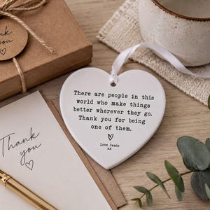 a heart-shaped ceramic ornament with a message, a note, and a mug on a wooden surface.