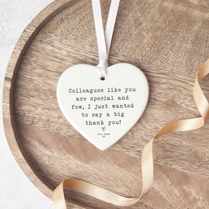 A heart-shaped ceramic ornament with a white ribbon hanging from it, placed on a wooden surface.