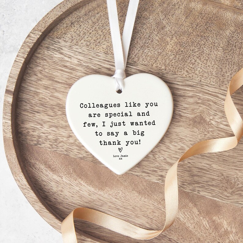 A heart-shaped ceramic ornament with a white ribbon hanging from it, placed on a wooden surface.