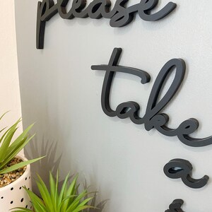 a wall with a decorative phrase "Please take a seat" in black cursive lettering.