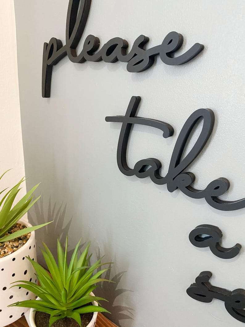 a wall with a decorative phrase "Please take a seat" in black cursive lettering.