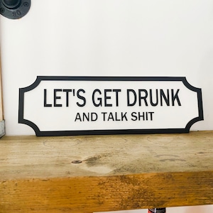 Könnte beinhalten: Ein schwarz-weißes Schild mit abgerundeten Ecken und schwarzem Rand. Das Schild lautet "Let's Get Drunk and Talk Shit".