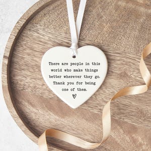A heart-shaped ceramic ornament with a ribbon tied around it, placed on a wooden surface.