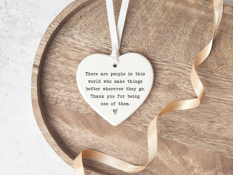 A heart-shaped ceramic ornament with a ribbon tied around it, placed on a wooden surface.