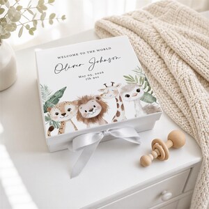 May include: A white square keepsake box with a satin ribbon closure, featuring the text Welcome to the World, Oliver Johnson, May 05, 2026, 7lb 9oz, and illustrations of a leopard, lion, giraffe, and ostrich surrounded by green tropical leaves.