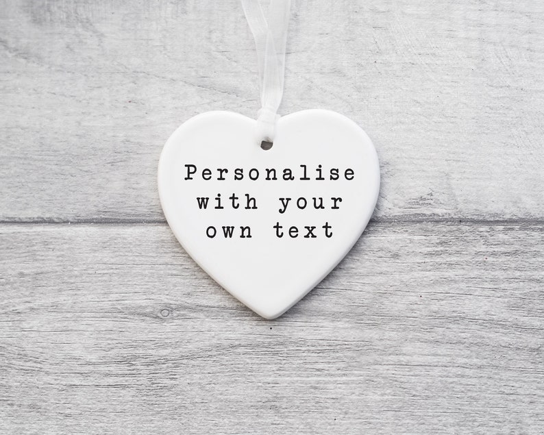 May include: White ceramic heart-shaped ornament with a white ribbon. The ornament has the text "Personalise with your own text" printed on it.