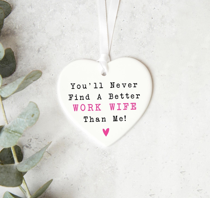 May include: White ceramic heart-shaped ornament with the text "You'll Never Find A Better WORK WIFE Than Me!" in black and pink lettering.