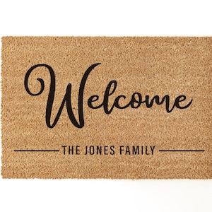May include: A brown coir doormat with the text "Welcome" in a black cursive font. Below the text is a line with the text "The Jones Family".